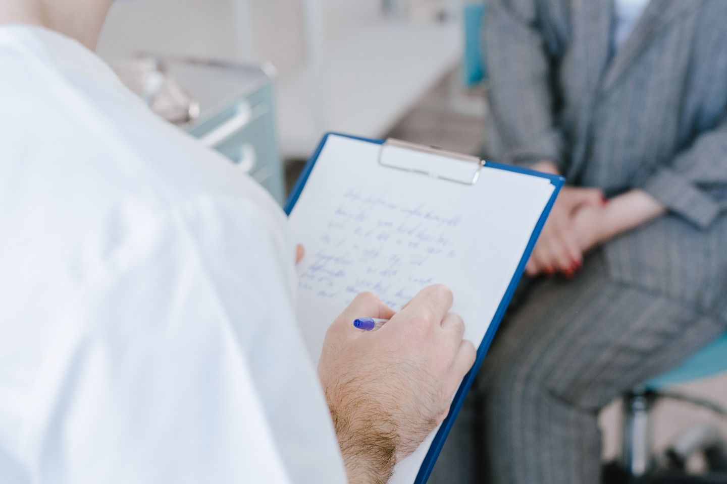 A healthcare professional writing notes on a clipboard during a consultation