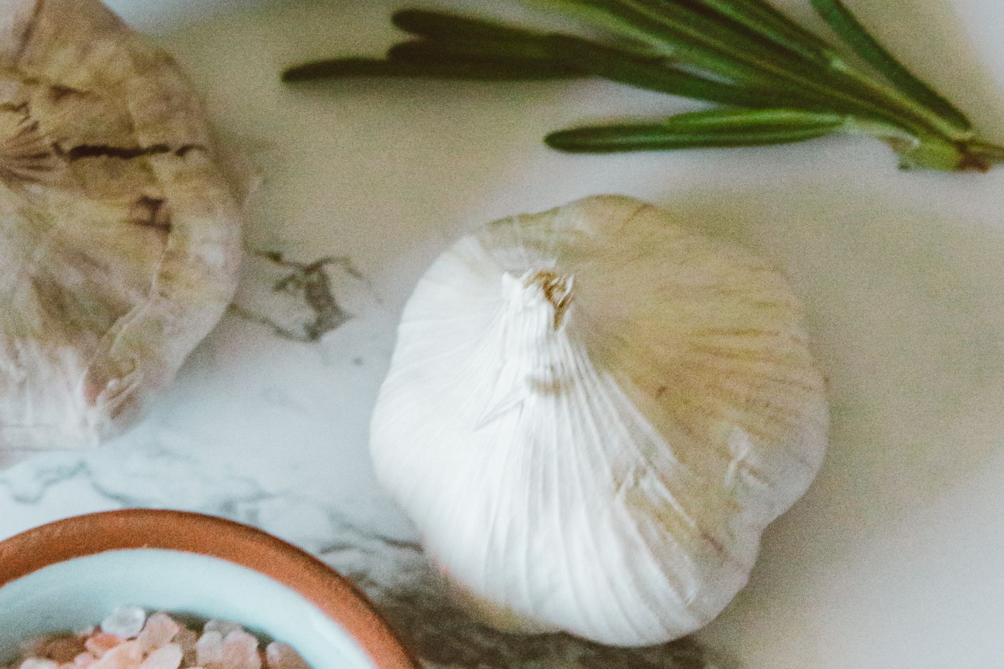 A garlic bulb, herbs and a bowl of pink salt arranged on a kitchen surface